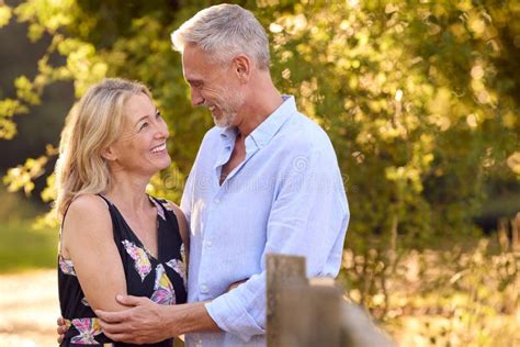 Loving Mature Couple Leaning On Fence On Walk In Countryside Together