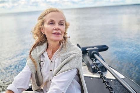 Une blonde mature woman in white clothes assis sur un bateau et à la rêveuse Photo Premium