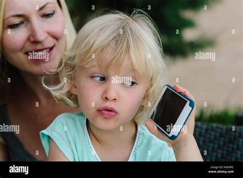Petite fille blonde assise sur les genoux de sa mère et de jouer avec un smartphone Photo Stock