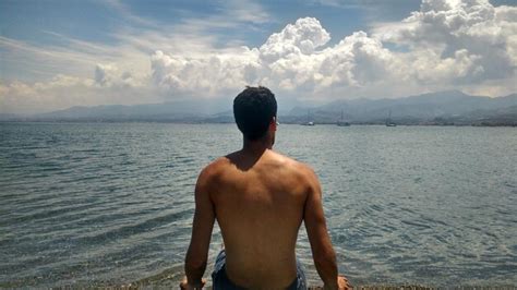 Vista Traseira De Um Homem Sem Camisa Sentado Na Praia Contra O C U