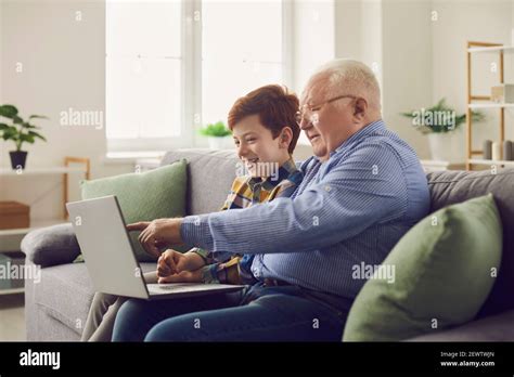 Grandfather And Grandson Sitting On Sofa With Laptop And Watching Movie