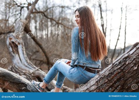 Young Beautiful Girl In Denim Jacket And Jeans Sits On A Tree An Stock