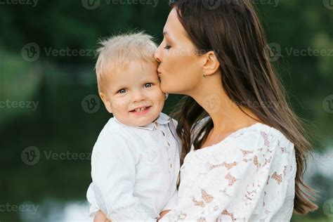 A Mother Kisses Her Two Year Old Son The Son Is Happy And Smiling