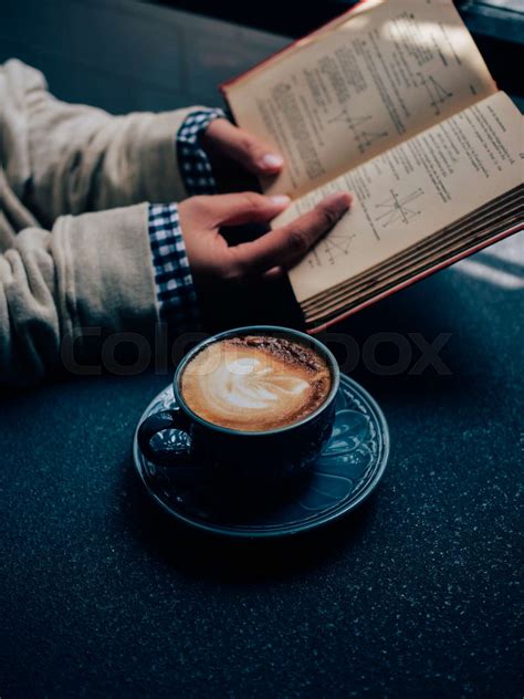 Close up Woman hands reading a book and drinking coffee in coffee shop ...