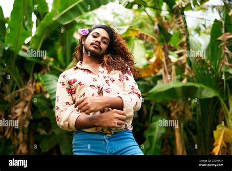 South Asian Man With Flower In Hair Stands Confidently In Lush Garden Expresses Gay Pride
