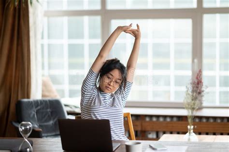 Tired Young Asian Woman Sitting At The Laptop And Stretching Her Arms