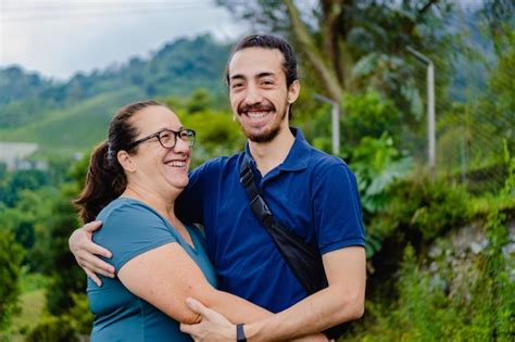 Madre Latina Abrazando A Su Hijo Joven Con Barba Afuera En El Bosque Sonriendo Con Amor Foto