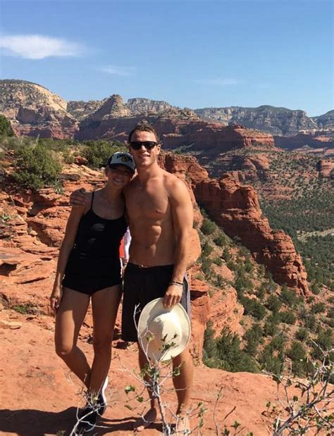 A Man And Woman Standing On Top Of A Rocky Cliff With Mountains In The