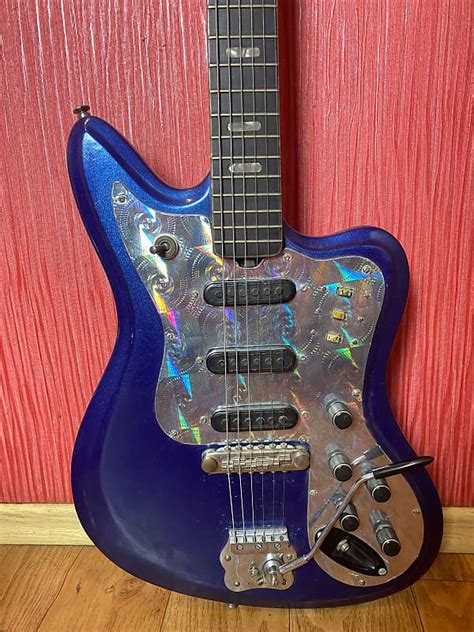 A Blue Electric Guitar Sitting On Top Of A Wooden Floor Next To A Red Wall