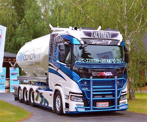 A Large Blue And White Truck Driving Down A Road Next To Some Trees In