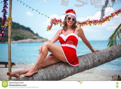 Cute Blonde Woman In Red Dress Sunglasses And Santa Hat Sitting On Palm Tree At Exotic Tropical