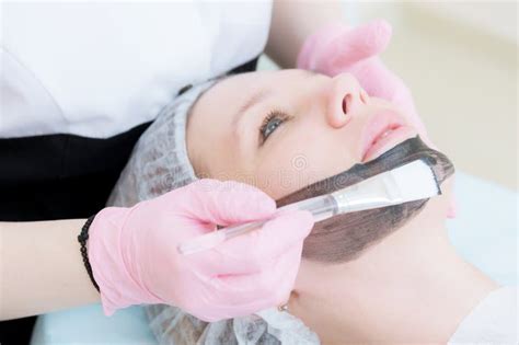 The Cosmetologist In Pink Gloves With A Brush Applies A Carbon Mask For