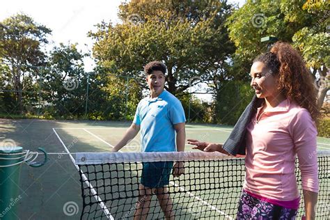 Smiling Biracial Couple Playing Tennis Talking Over The Net On Sunny