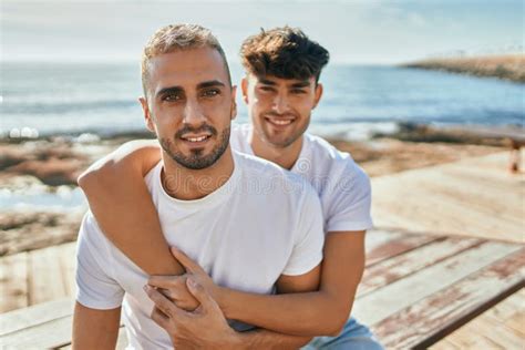Jovem Casal Gay Sorrindo Feliz Sentado No Banco No Palco Da Praia Foto De Stock Imagem De