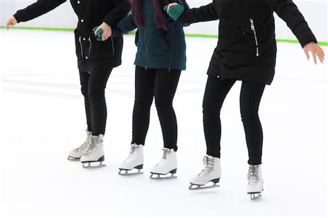 Três garotas de mãos dadas patinando no gelo na pista de gelo