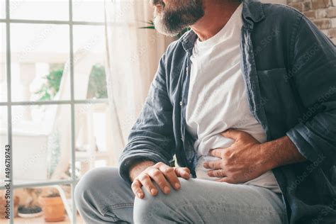 Man Suffering With Severe Stomach Pain Sitting At Home Hand Of Mature