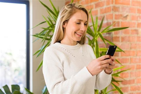 Hübsche blonde Frau des jungen Erwachsenen zu Hause ihr Smartphone verwendet Premium Foto