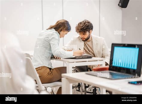 Brunette Female Employee Working Together With Her Good Looking Handicapped Male Colleague In
