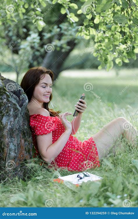 Plus Size Girl Sitting On Grass Under Tree And And Using Her Smartphone