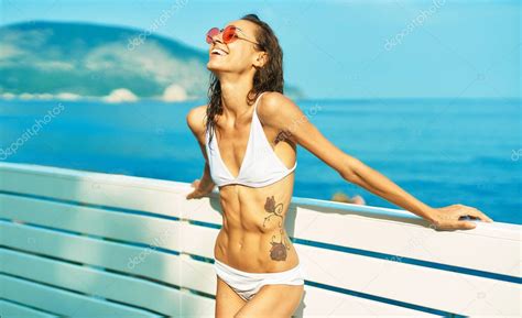Mujer Feliz Bronceada Con Cuerpo En Forma En Bikini Blanco Y Gafas Rojas Posando A Orillas Del