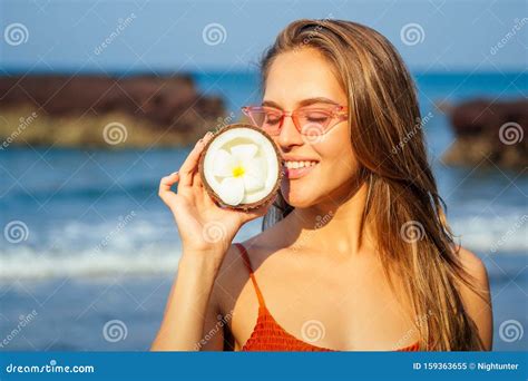 Mujer En Bikini De Coral Naranja Y Gafas Rosas Frescas Paradas En La Playa Con Cocos Abiertos