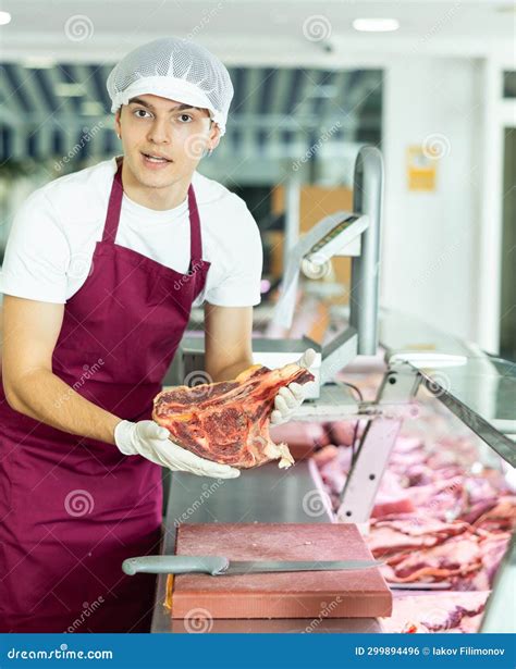 Positive Young Salesman Demonstrating Piece Of Meat In Butcher Shop