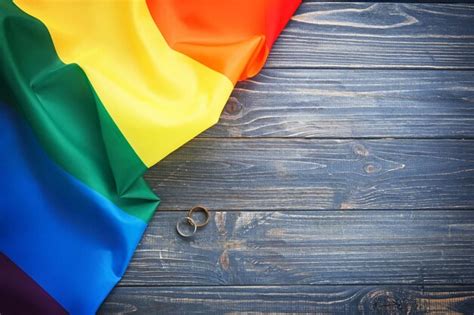 Dos Anillos De Boda Y La Bandera Gay Del Arco Iris Sobre Fondo De Madera Foto Premium