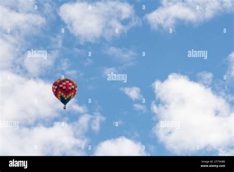 An Isolated Multicolored Hot Air Balloon Floats In The Air With White Clouds And A Crisp Blue