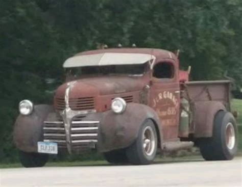 An Old Truck Is Parked On The Side Of The Road In Front Of Some Trees