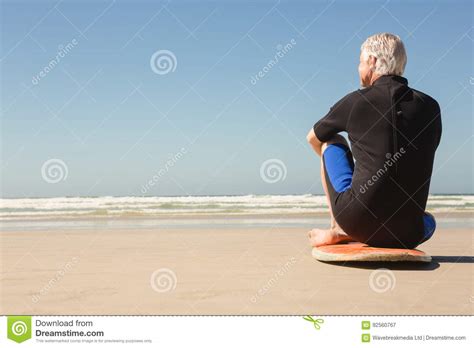 Senior Man Sitting On Surfboard At Beach On Sunny Day Stock Image