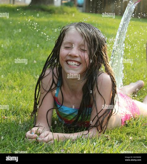 young girl laying n grass on stomach enjoying cool water on hot summer ...