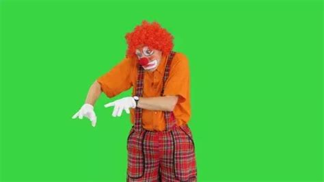 a man in clown makeup and red hair is dancing on a green screen