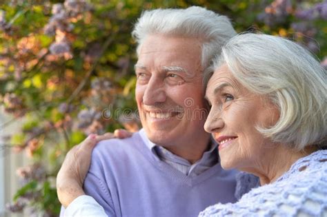 Portrait Of Beautiful Senior Couple Hugging In The Park By Lilacs Stock