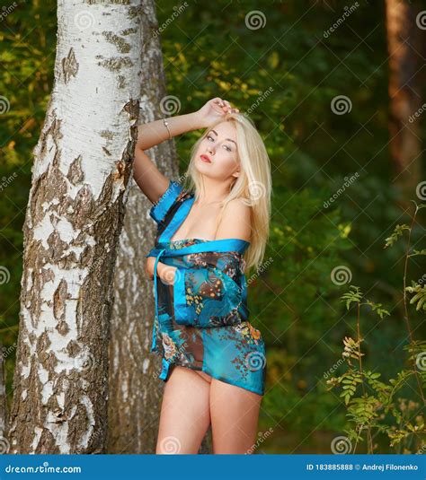 Naked Tanned Blonde In A Blue Cape Poses In The Forest Leaning On A Tree Youth Female Beauty
