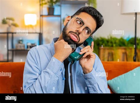 Irritated Young Indian Man Talking On Vintage Retro Wired Telephone At Home Apartment