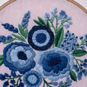 An Embroidery Project With Blue Flowers And Green Leaves On Pink Fabric