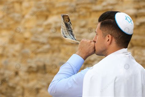 Jewish Man In Kippah And Tallit Blowing Shofar Outdoors Rosh Hashanah