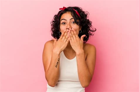 Jovem mulher latina encaracolada isolada em fundo rosa chocada cobrindo a boca as mãos
