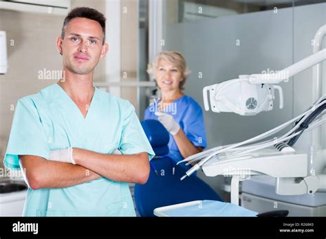 Male Dentist Standing In Dental Office With Hands Crossed Looking At