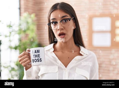 Young Brunette Woman Drinking From I Am The Boss Coffee Cup Scared And