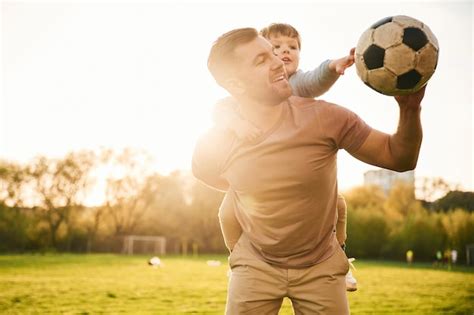 Sobre los hombros con la pelota de fútbol padre feliz con el hijo se