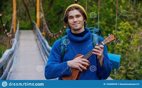 Young Smiling Man Standing On The Bridge And Playing Ukulele Stock