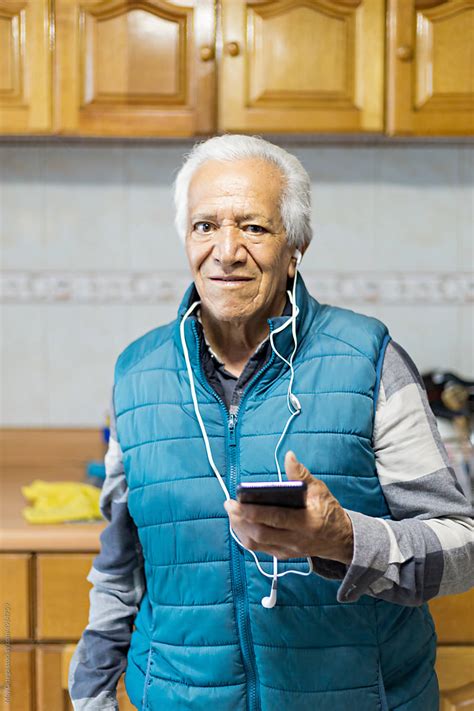 Portrait Of Elderly Man Looking At Camera Using Mobile Phone By