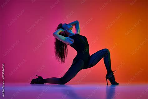 Flexibility and passion. Young woman dancing high heel, contemp dance over gradient pink red ...