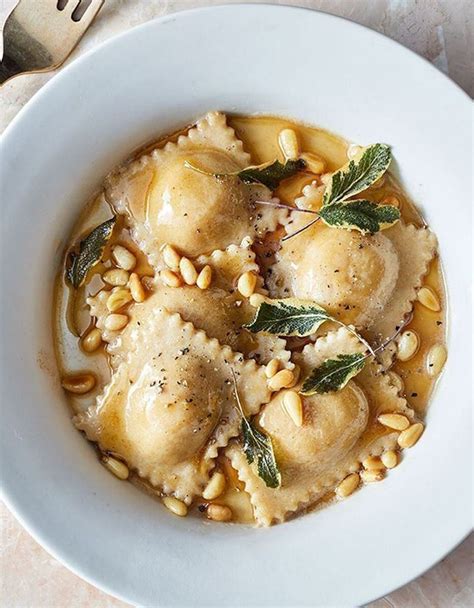 A White Plate Topped With Pasta And Meat Covered In Gravy Garnished With Green Leaves