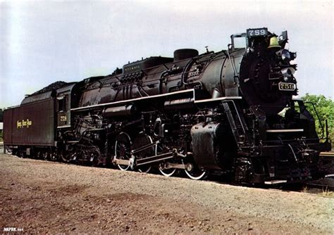 An Old Black Train Is Parked On The Tracks In Front Of Some Grass And Trees