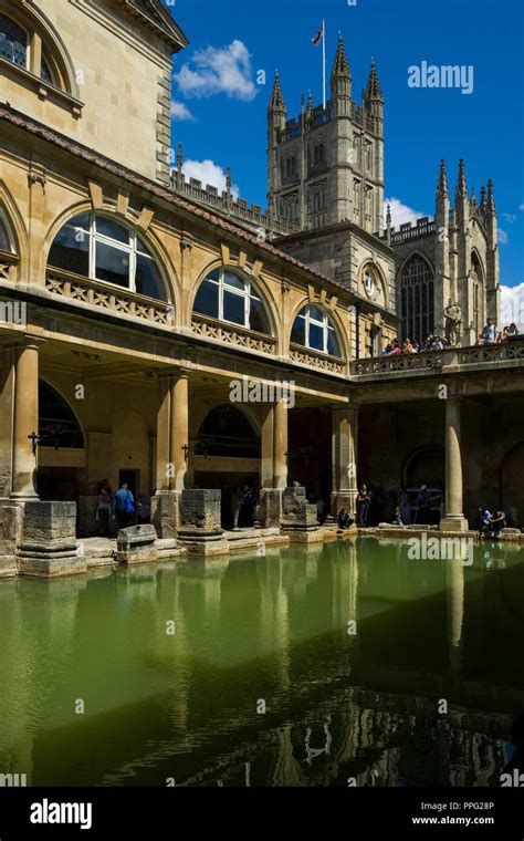 Visitors Exploring The Historic Roman Baths With Bath Abbey Towering