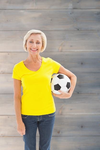 Premium Photo Mature Blonde Holding Football Smiling At Camera Against Pale Grey Wooden Planks