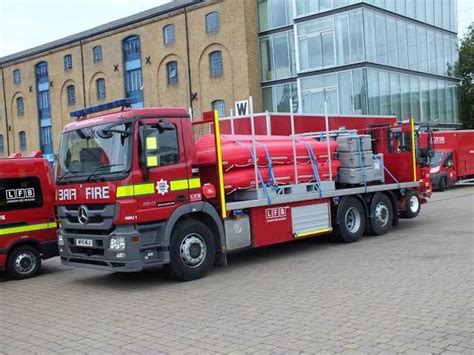 Two Red Fire Trucks Parked Next To Each Other In Front Of A Tall Brick