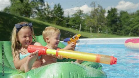 CLOSE UP: Smiling little children aiming and splashing with water guns ...